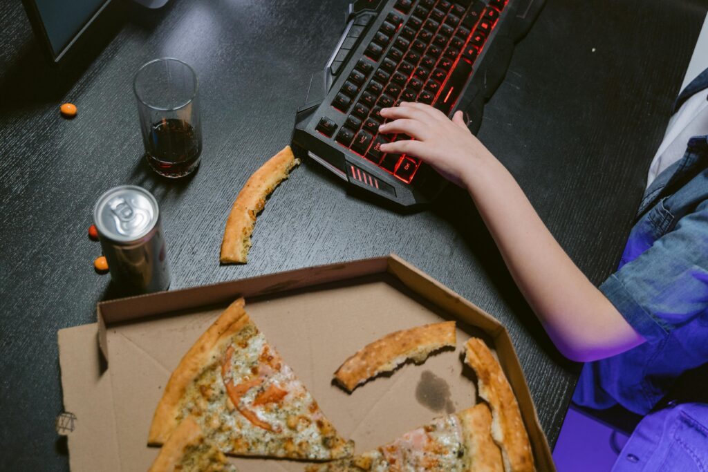 Teen immersed in gaming with drinks and pizza on the desk, perfect for gaming and lifestyle themes.