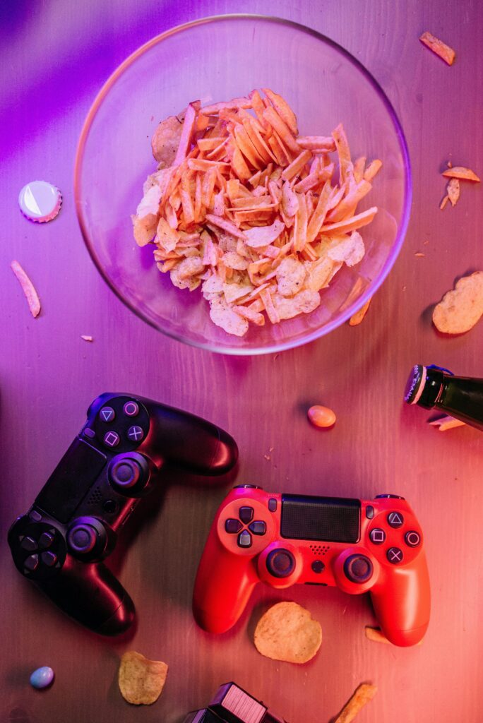 Top view of a bowl of chips surrounded by gaming controllers on a wooden surface.